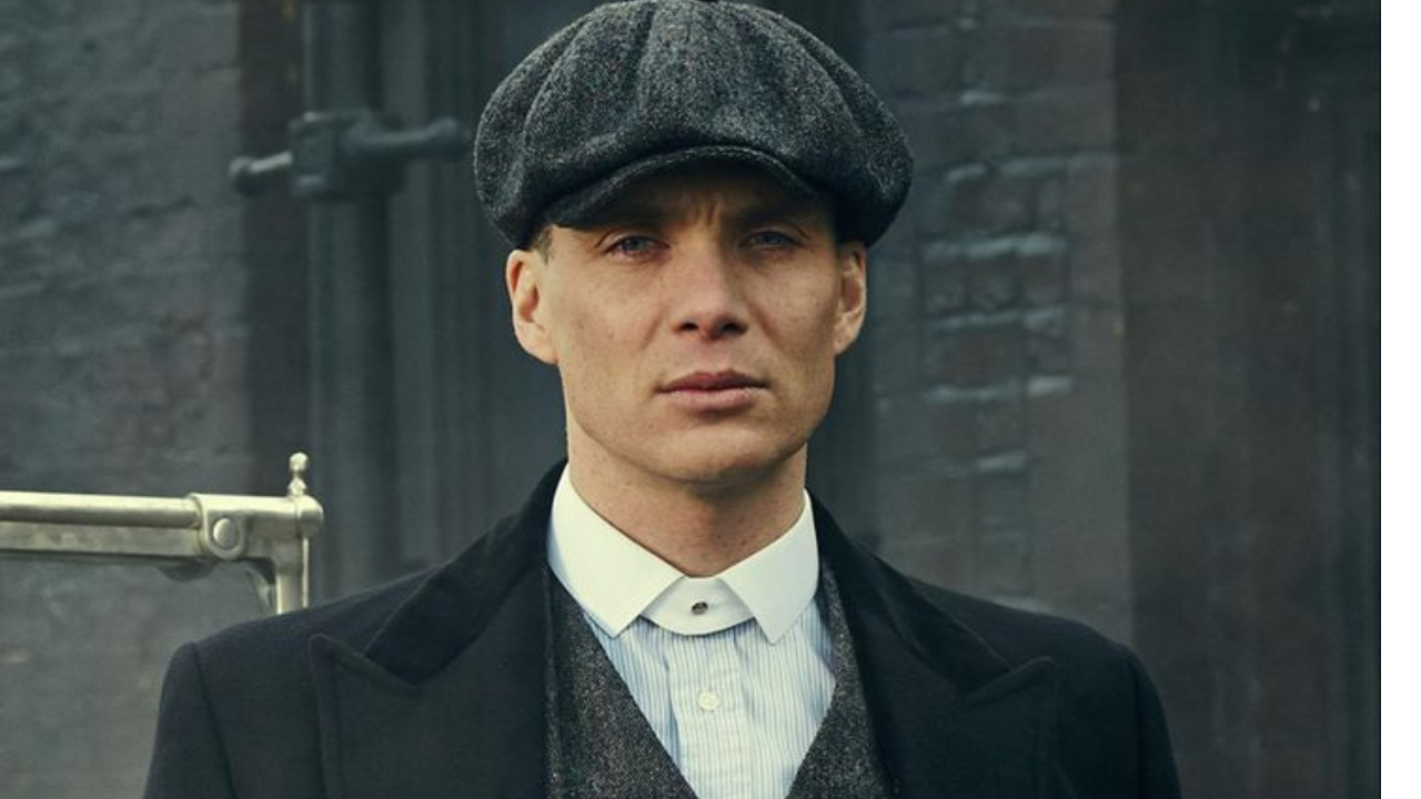 A stylish man in a hat and coat posing in front of a historic building.